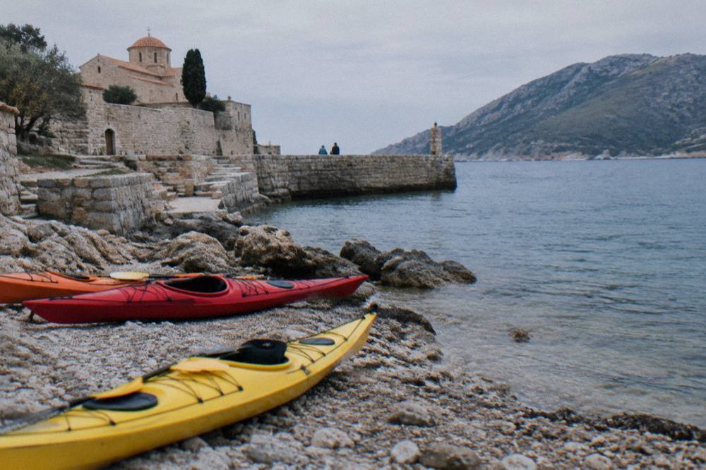 Kayaks resting on a rocky shore near a historic stone harbour wall