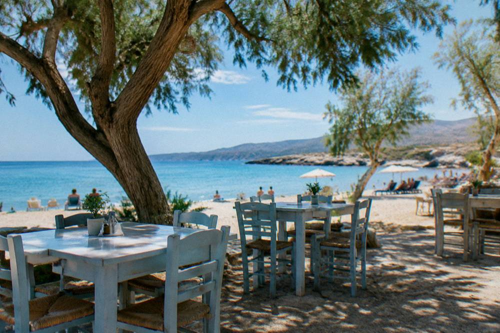 Taverna tables under trees near the sand at Kalathas Beach