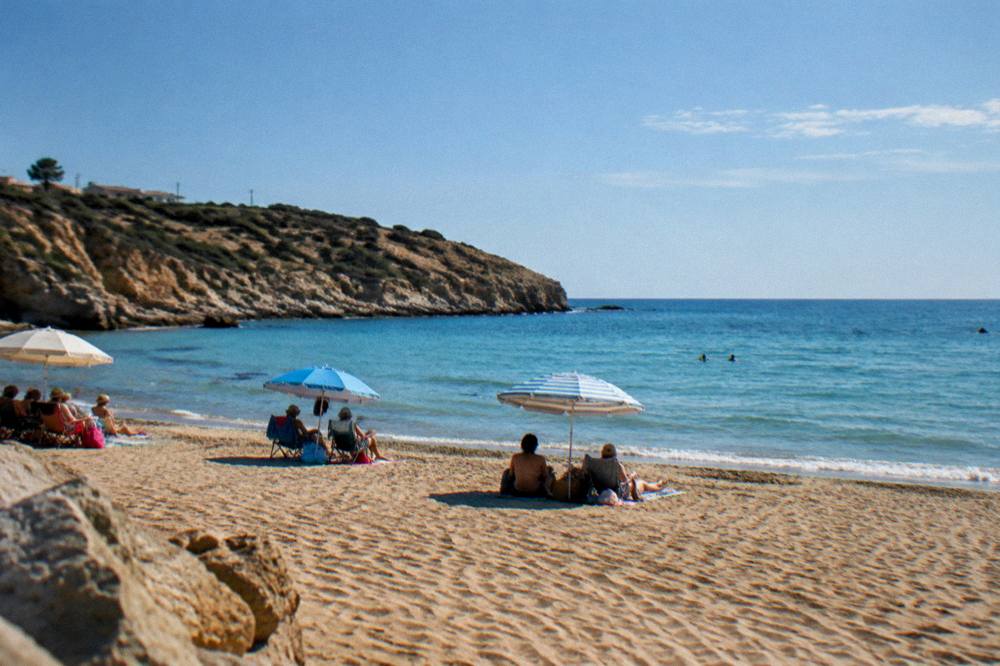 Families under umbrellas on the sand at Kalathas Bay in late afternoon light