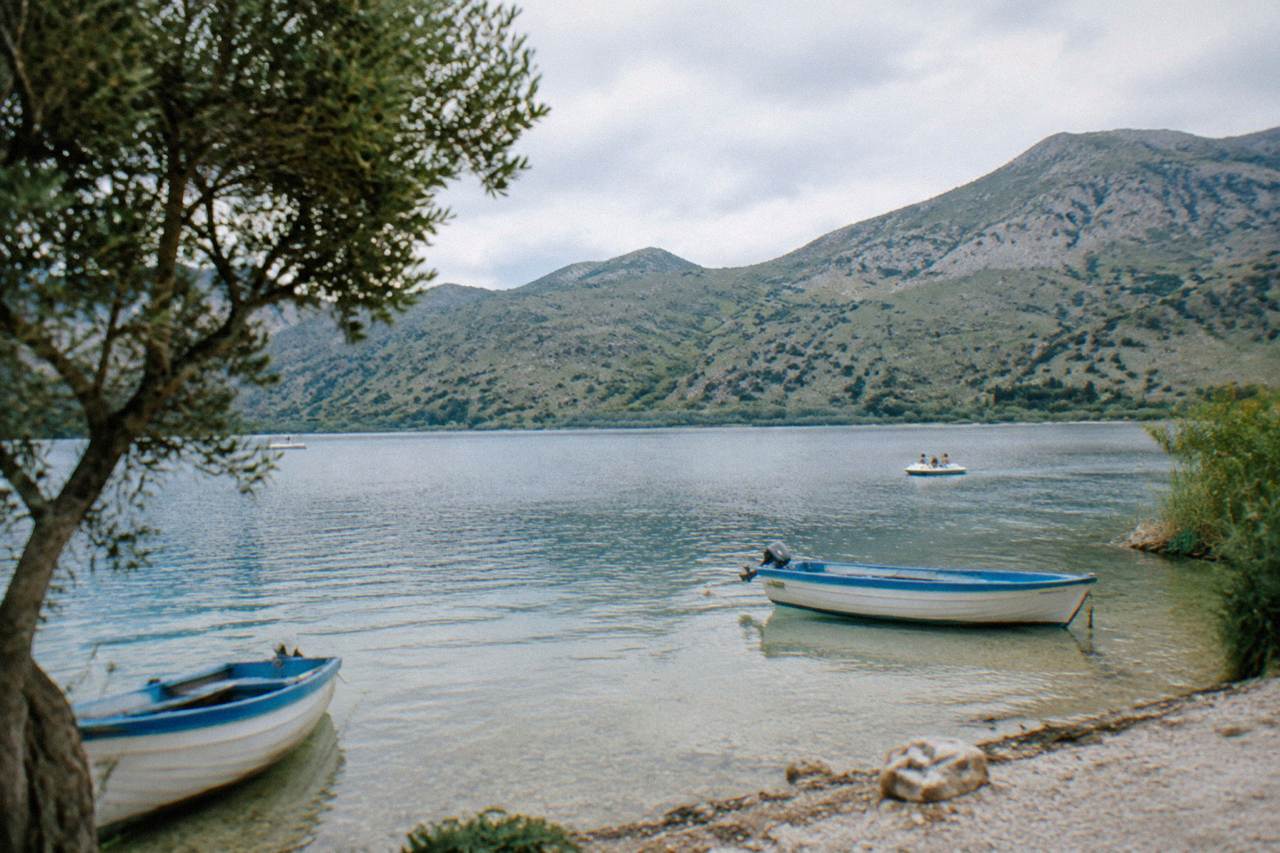 A calm freshwater lake ringed by green hills with a few small boats at the shore