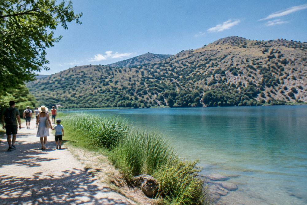 Families walking together along a flat lakeside path with hills behind calm water