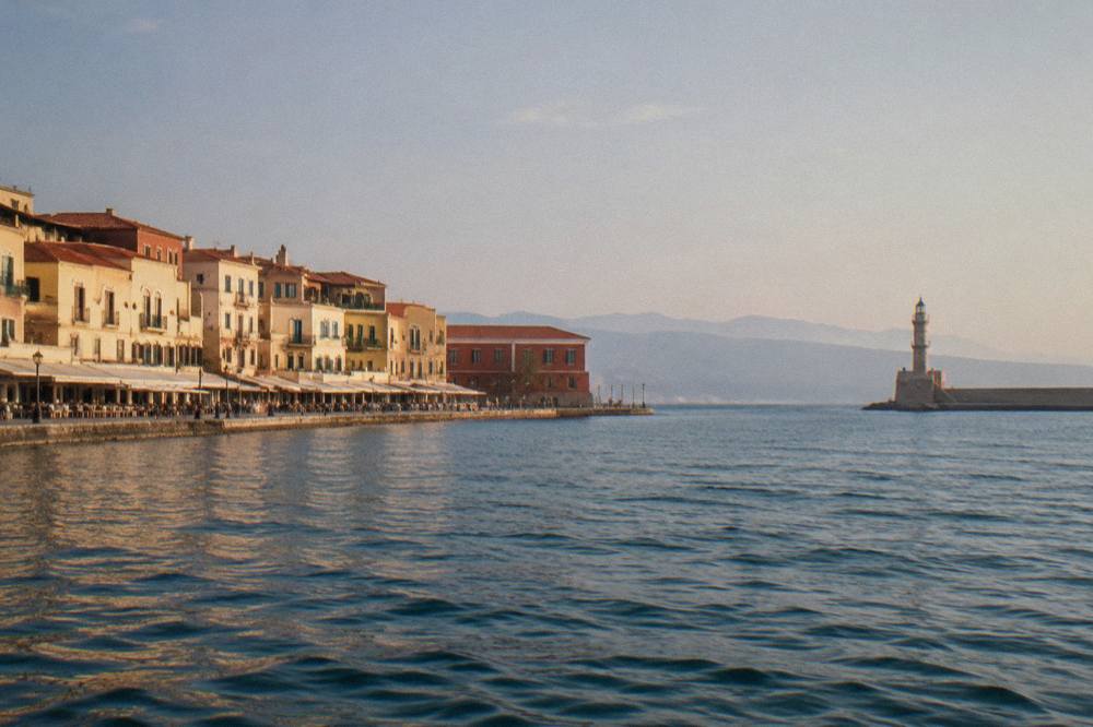 The Venetian Harbour of Chania seen from the water, with pastel buildings along the quay and a lighthouse at the far point