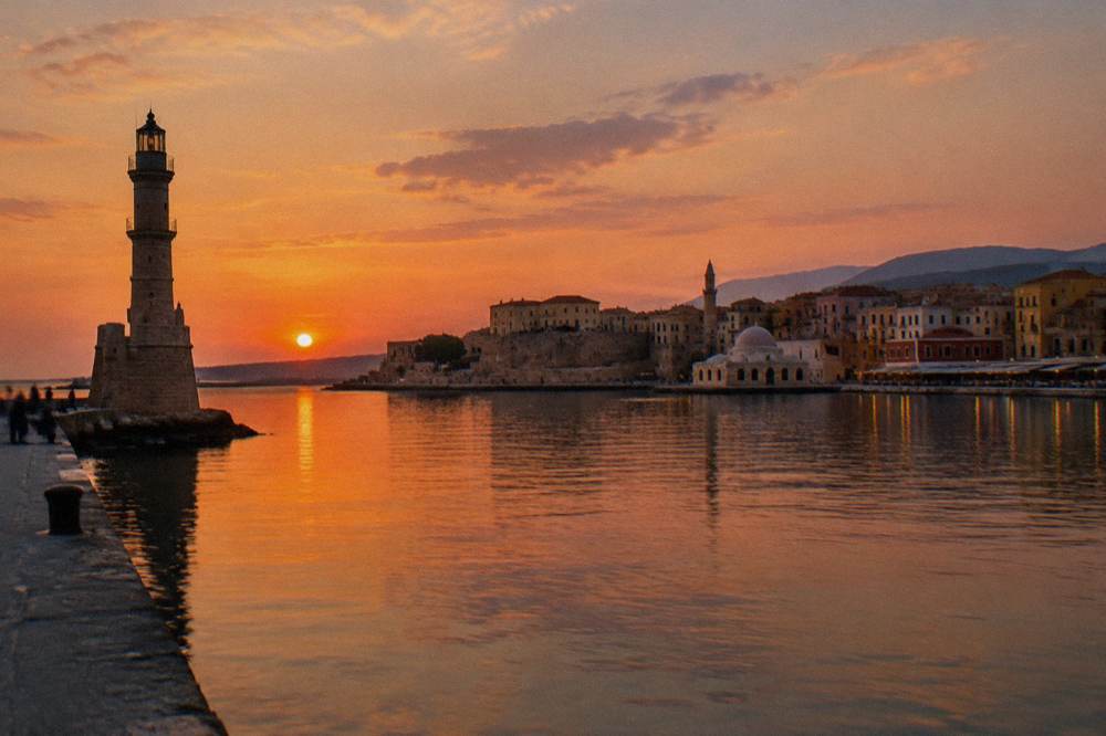 A panoramic view across a curved harbour with old stone buildings, domes and a minaret, seen from a mole at dusk