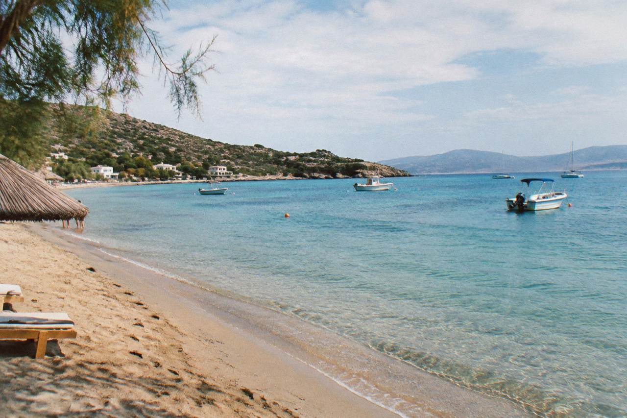 A calm sandy beach with shallow turquoise water and a few small boats anchored offshore
