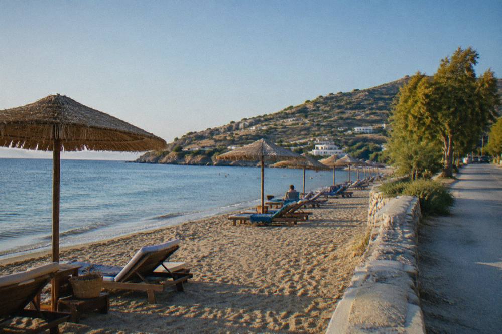 Sun umbrellas and sunbeds on a small sandy beach beside a quiet coastal road
