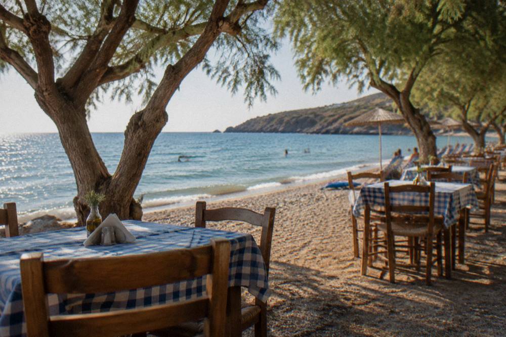 Wooden taverna tables set close to the sand under tamarisk shade