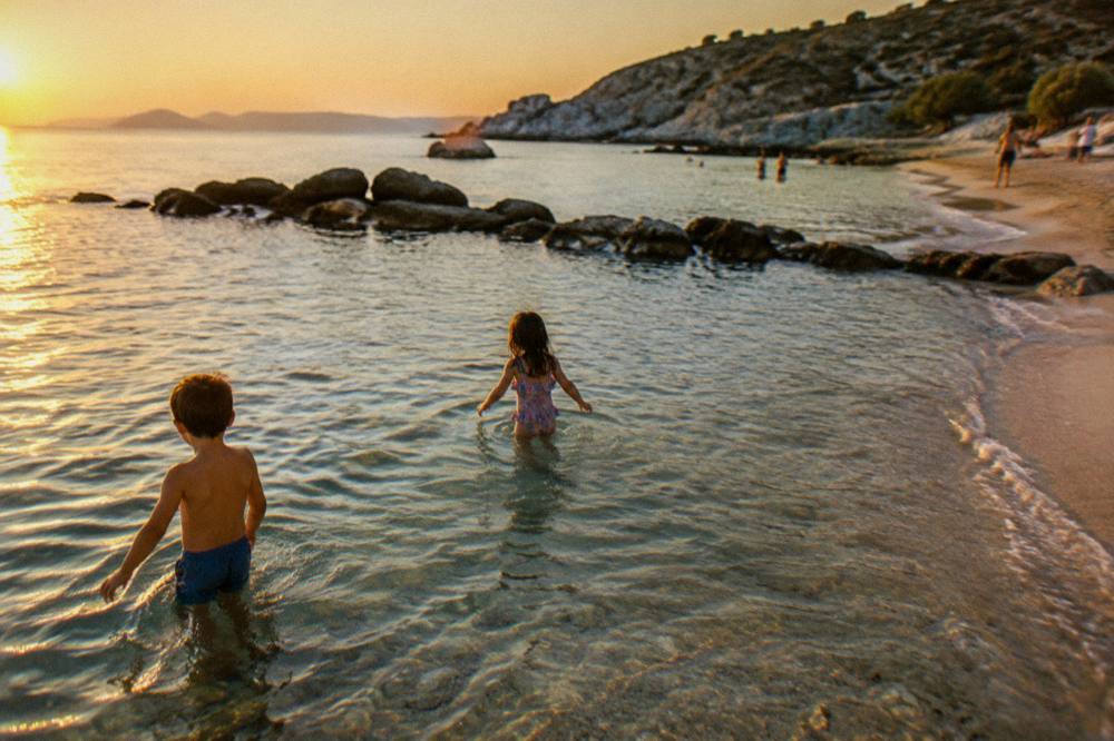 Children playing in shallow clear water beside a sandy shoreline