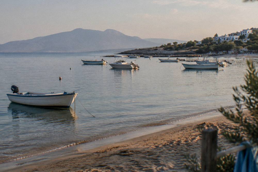 Small boats moored in a calm bay beside a sandy beach in late afternoon light