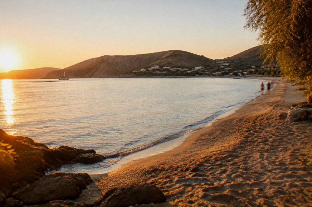 A quiet sandy bay at golden hour with calm water and hills in the distance
