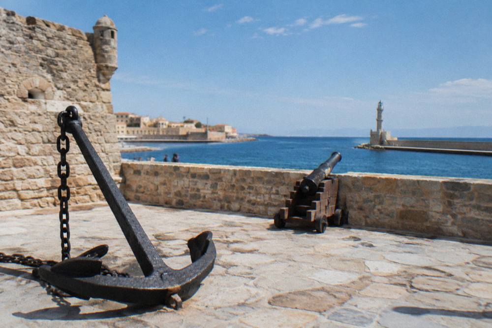 A low stone bastion of Firka Fortress above the sea with the harbour channel behind it