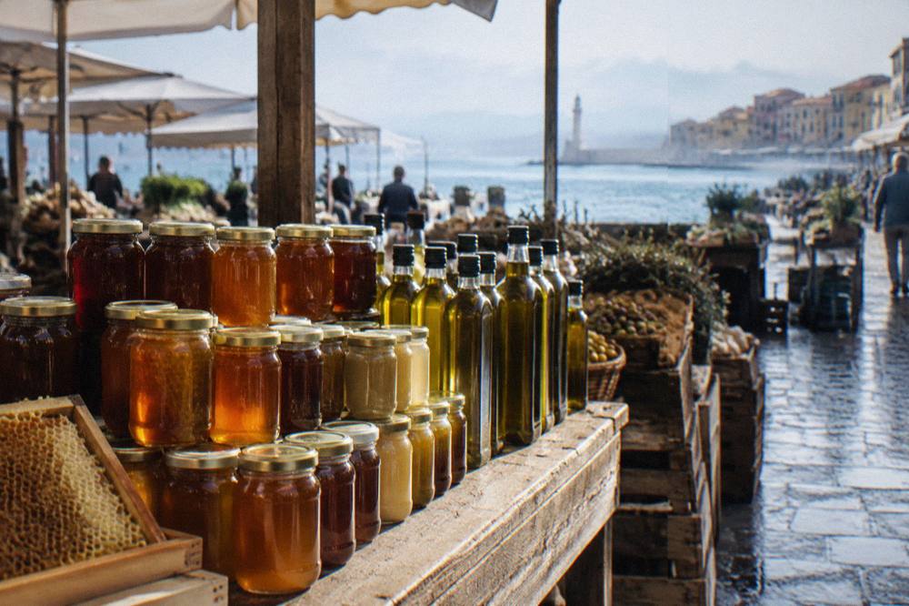 Jars of honey and bottles of olive oil lined up on a wooden market stall