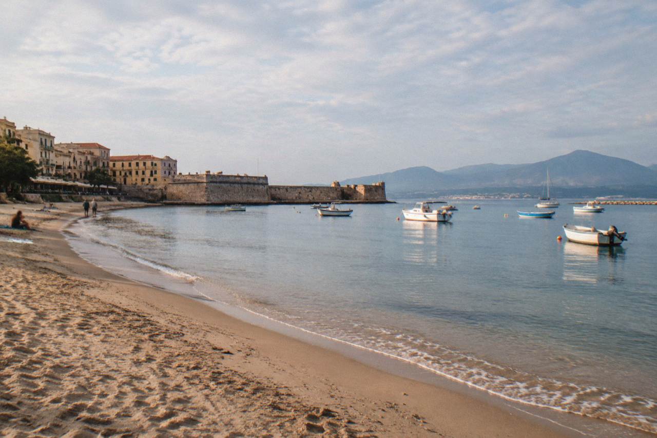 Sandy beach curving along a calm bay with an old stone pier and small boats at anchor