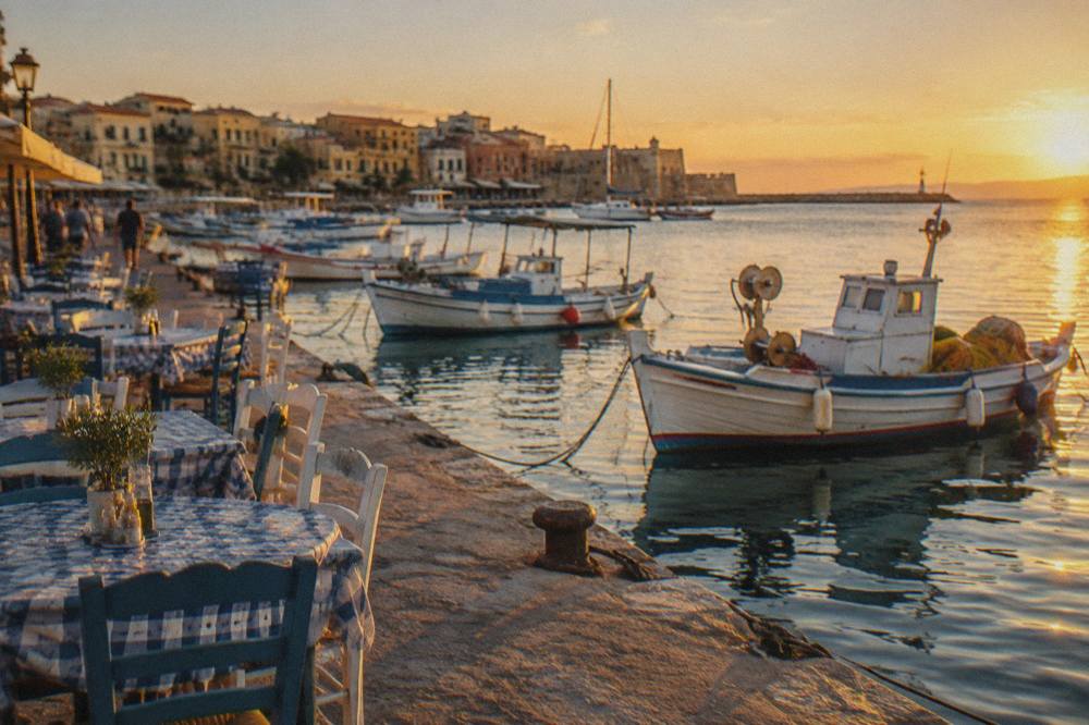 Small fishing boats moored in a harbour with taverna tables set out along the water
