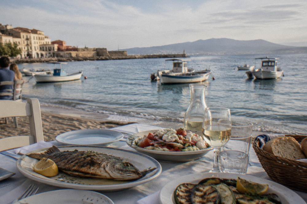 Table setting beside the water with grilled fish dishes and a view of small boats
