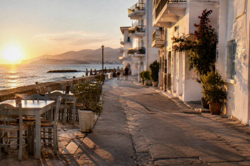Narrow residential street with white apartment buildings and taverna chairs near the seafront