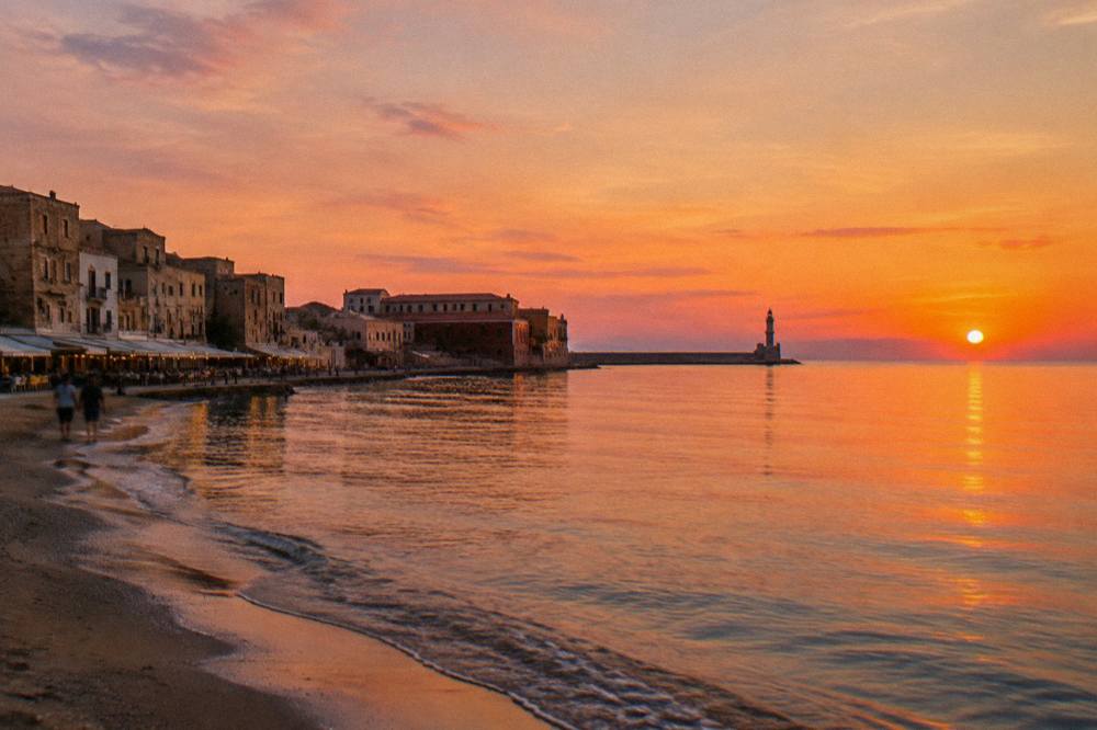 Harbour waterfront at dusk with stone buildings and a stone mole reaching into the sea
