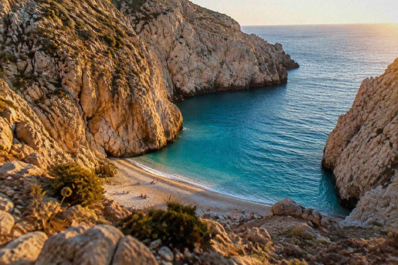 A narrow sandy cove at the bottom of steep pale cliffs above clear blue sea