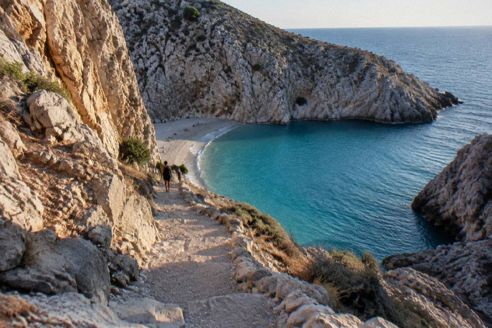 A steep rocky footpath winding down a pale cliff toward a small beach