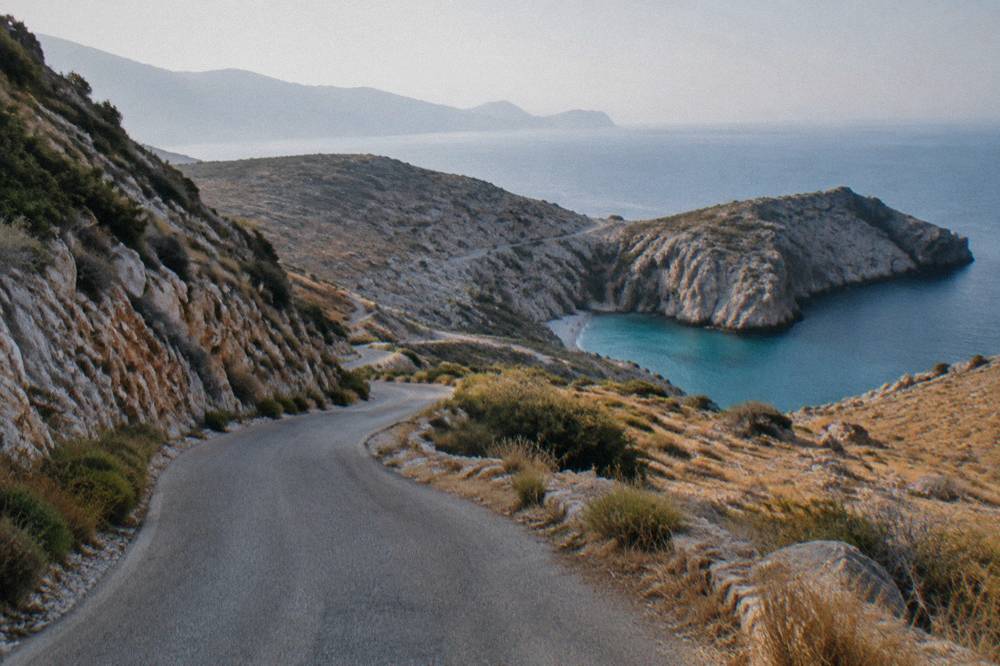 A winding narrow road across dry rocky peninsula landscape toward the sea