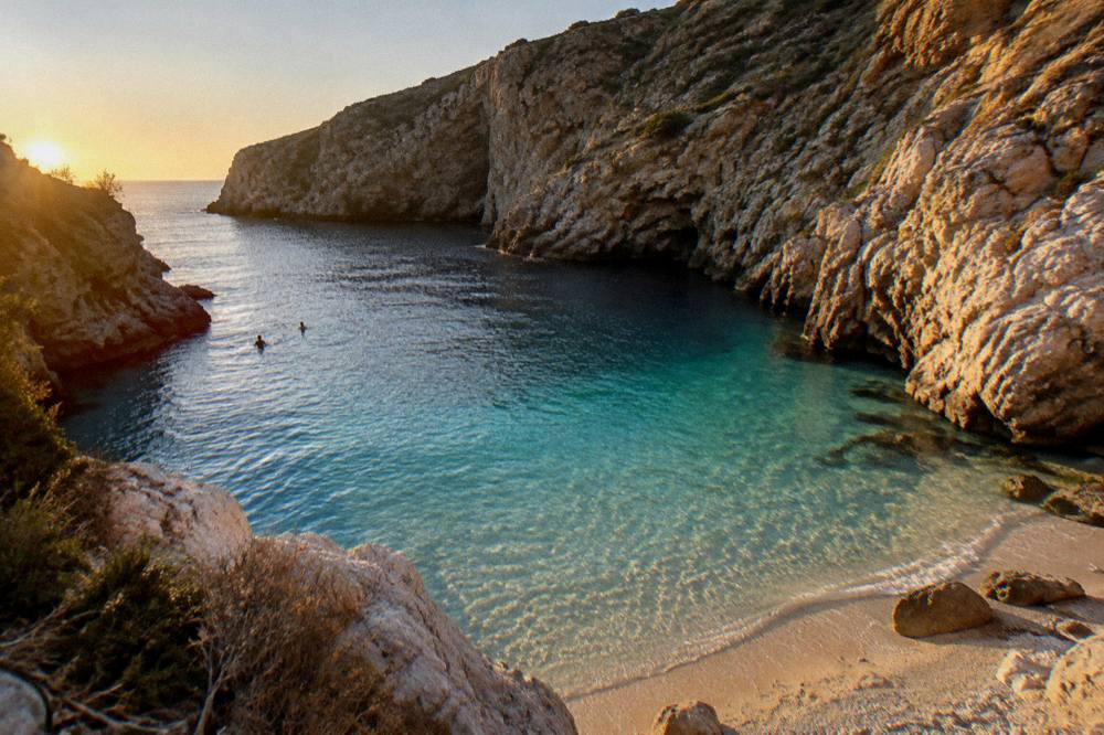 Shallow clear water over pale sand fading quickly into deep blue at a cliff cove