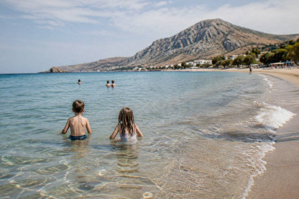 Children playing in shallow clear water at the edge of a sandy beach in Crete