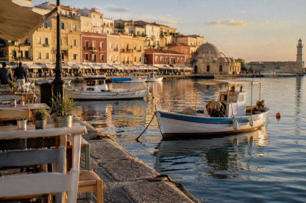 The inner quay of the Venetian Harbour with tables, boats and Old Town buildings behind them
