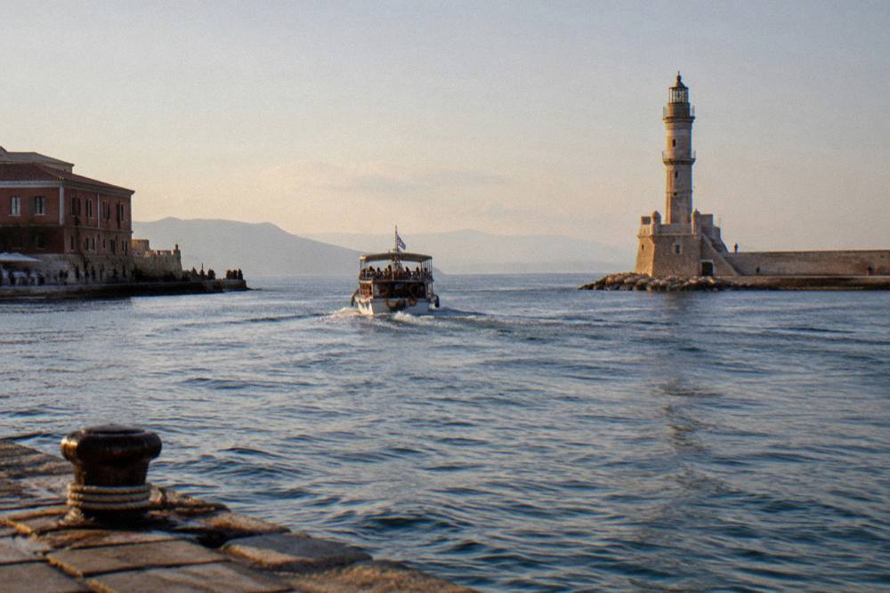 A small excursion boat departing the Venetian Harbour past the lighthouse in late afternoon light