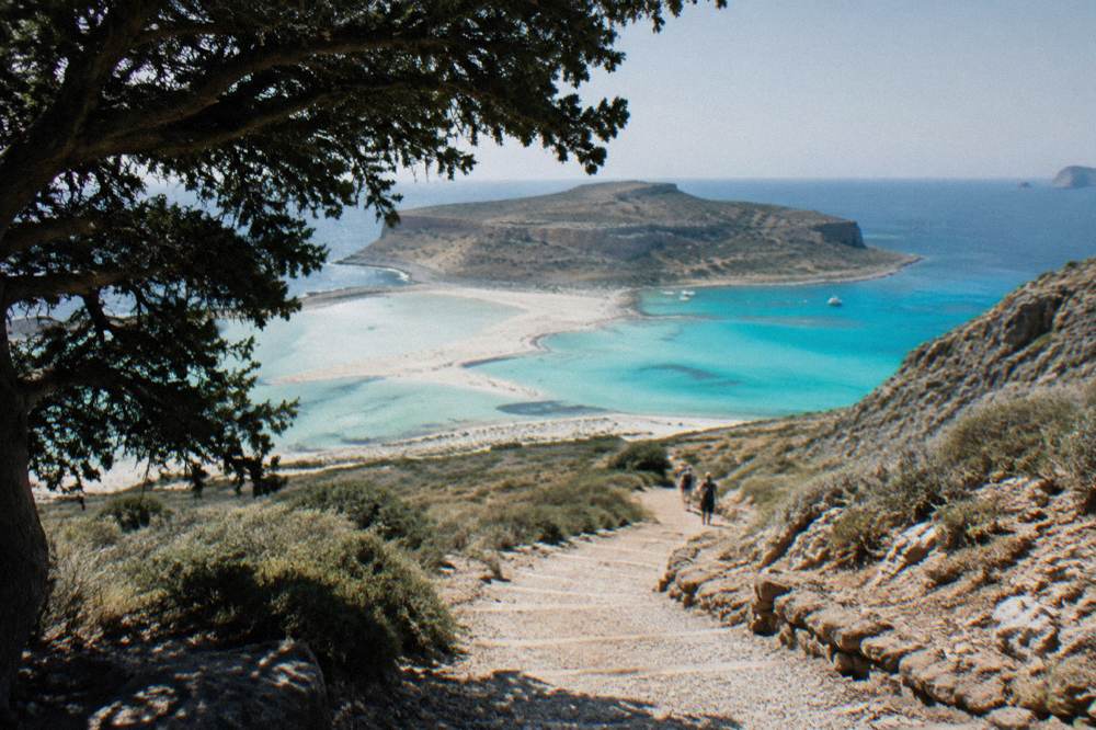 A gravel footpath zigzagging down a pale rocky slope toward a distant lagoon