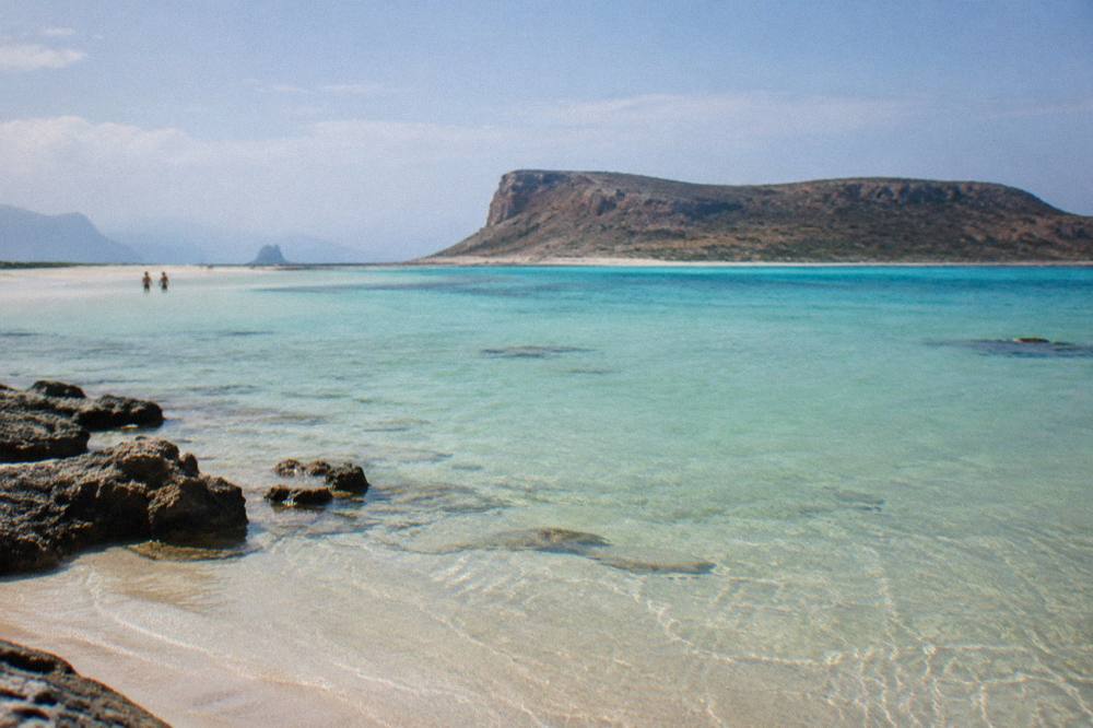 A calm lagoon at midday with shallow water lightening from blue to pale green over sand