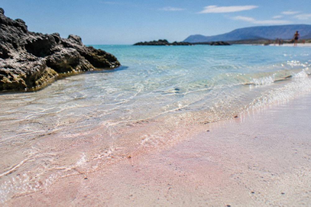 Close view of wet shoreline sand showing a faint pink tint mixed with pale grains