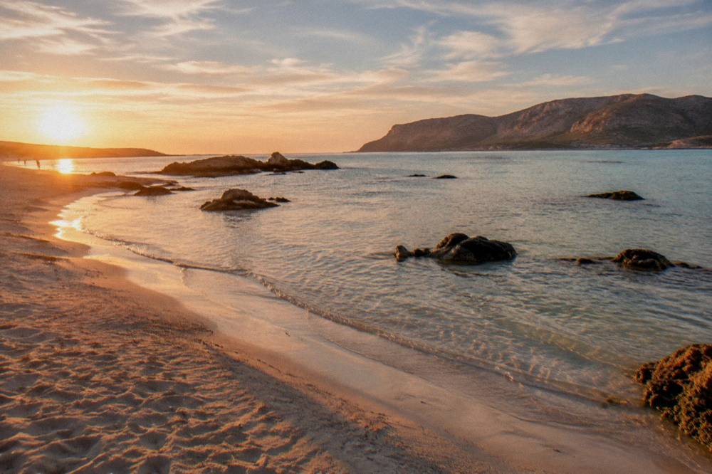 An empty beach at golden hour with long shadows across rippled sand and calm shallows