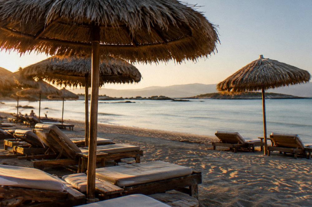 A shaded row of umbrellas on a sandy beach with calm shallow water beyond