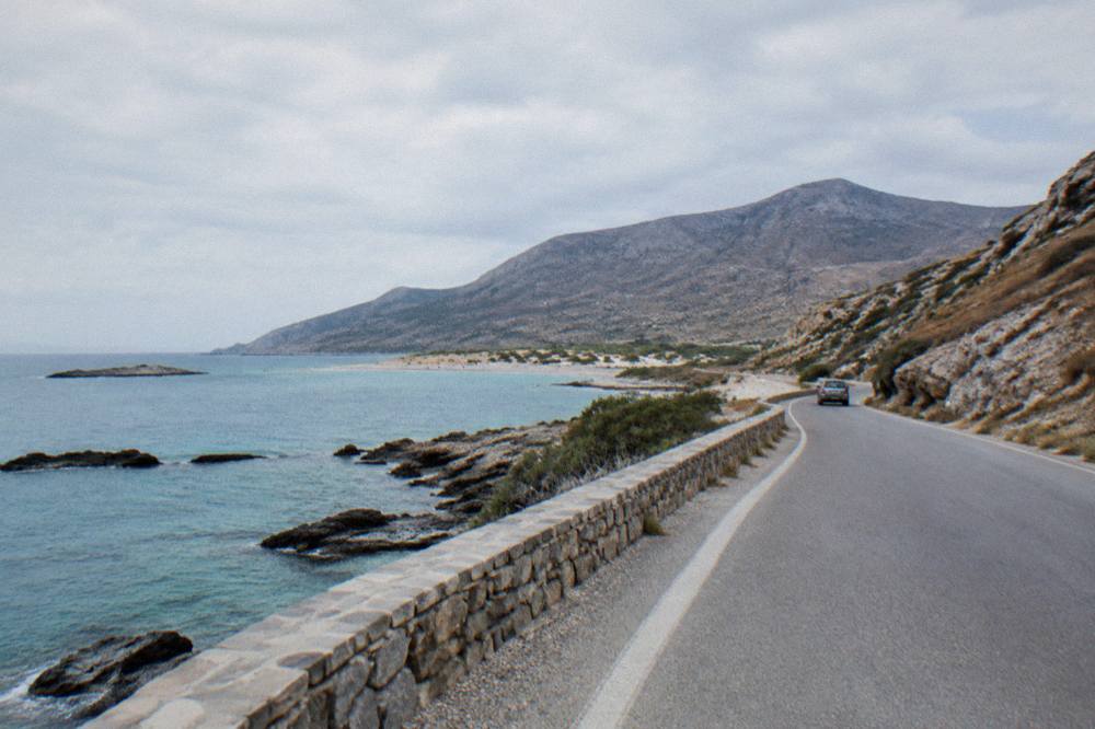 A coastal road curving between dry hills and the sea on a peninsula in western Crete