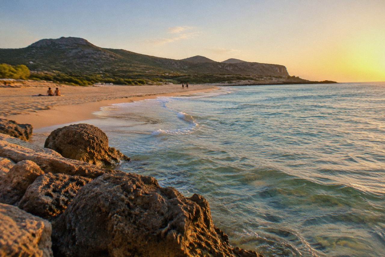 A wide sandy beach with clear shallow water and low green hills behind it
