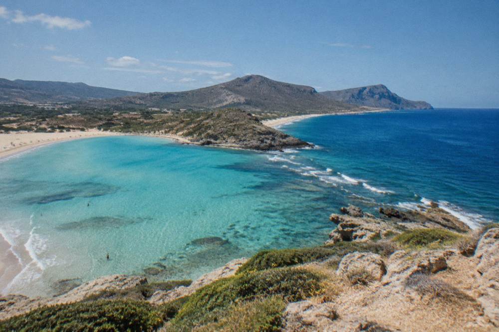 Two beaches compared from a headland, one with turquoise shallows and one with deeper blue water
