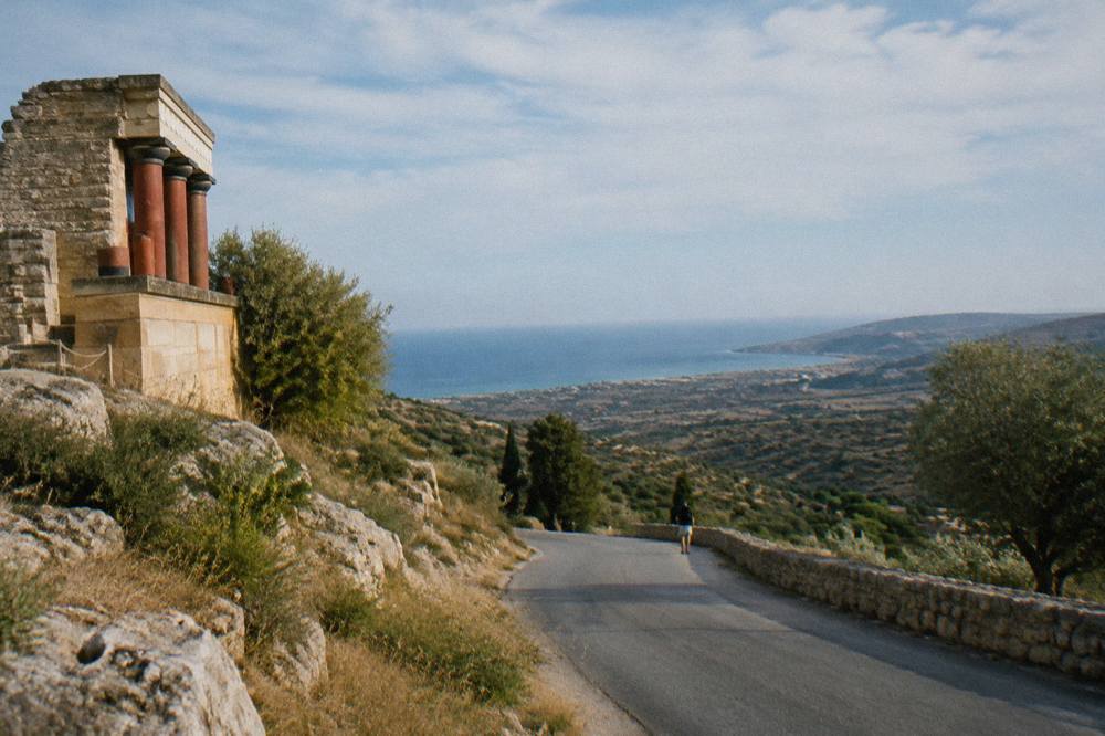 A long road crossing hilly Cretan countryside with the sea visible in the distance