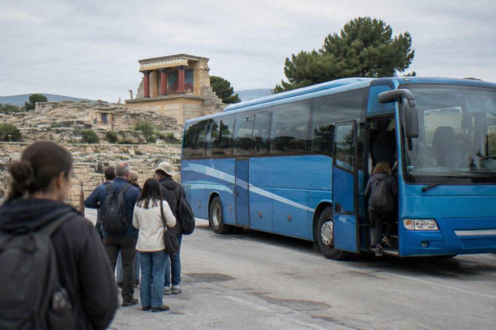 A blue intercity bus parked at a station with passengers waiting to board