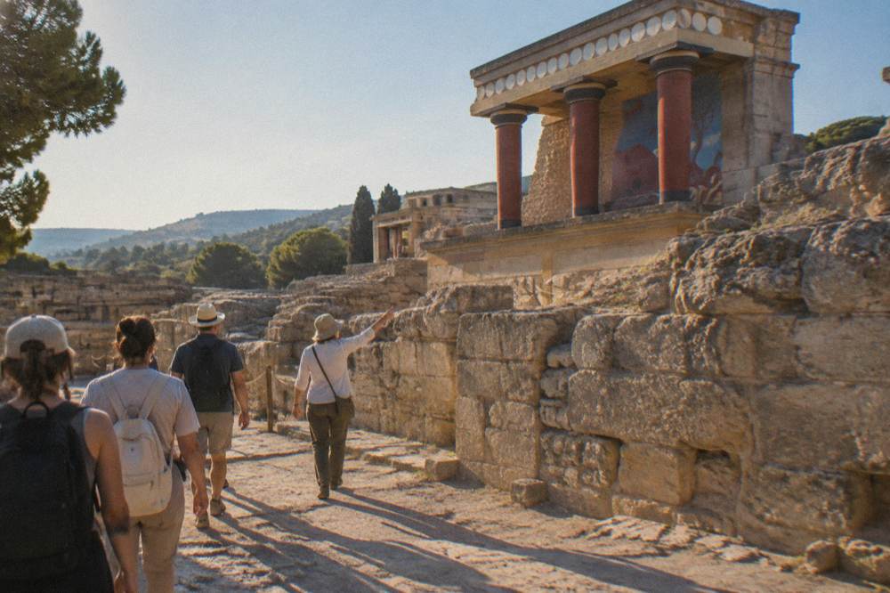 A group of visitors walking beside ancient stone walls with a guide pointing at the ruins