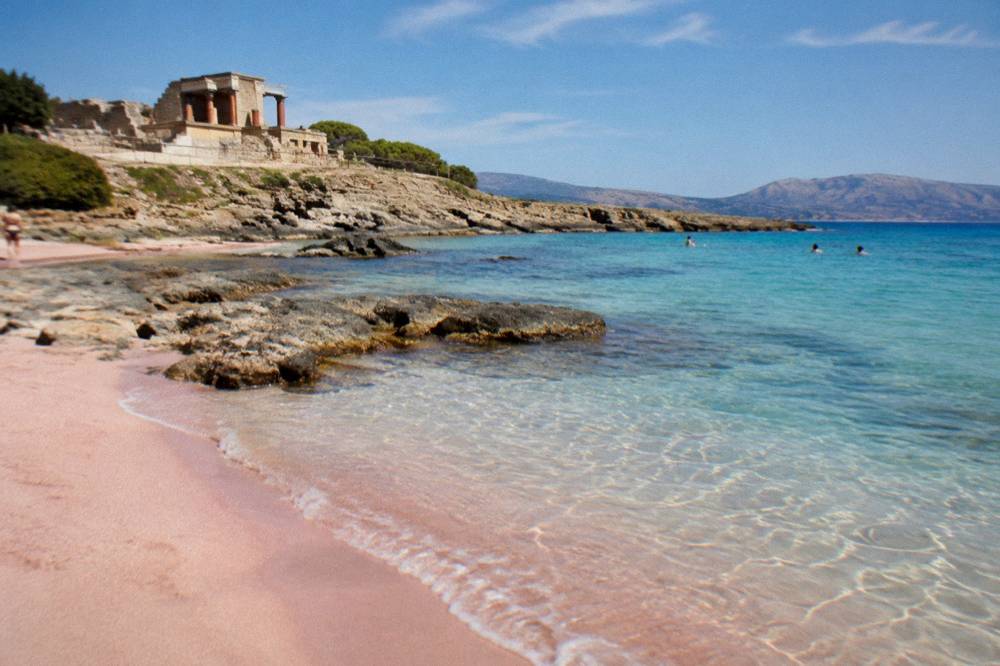 A pink-sand beach with shallow turquoise water at a protected Cretan shoreline