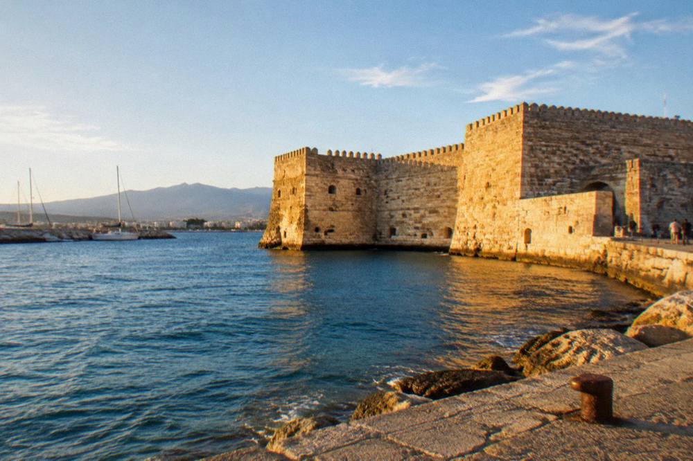 An old stone fortress wall at the edge of a harbour at golden hour