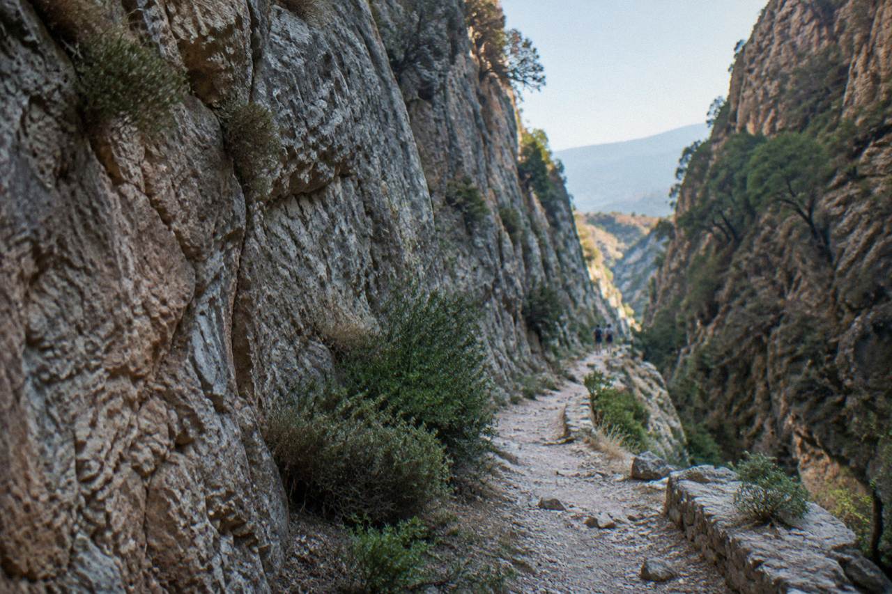 A narrow rocky gorge path winding between high stone walls under a clear sky