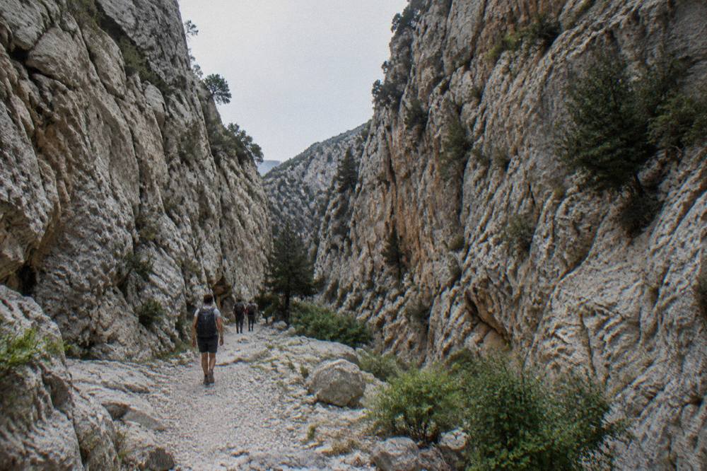 Walkers on a stony path between pale limestone walls inside a gorge
