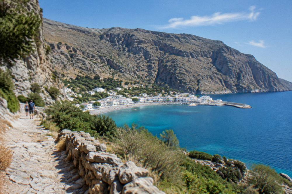 A small white village beside a deep blue bay at the foot of cliffs