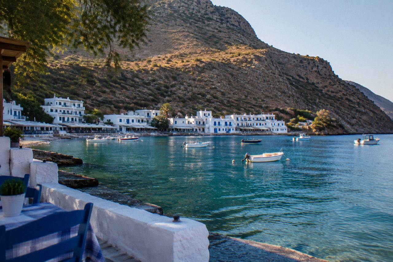 A small white village on a rocky bay with calm turquoise water and small boats moored offshore