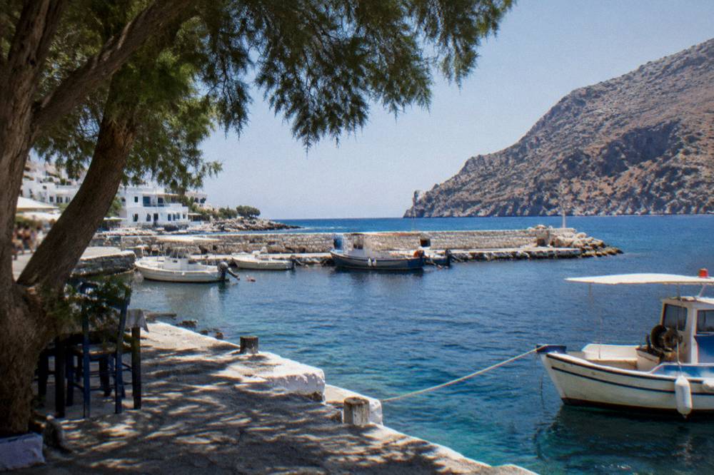 A stone harbour wall with moored boats under a clear summer sky above dark blue sea