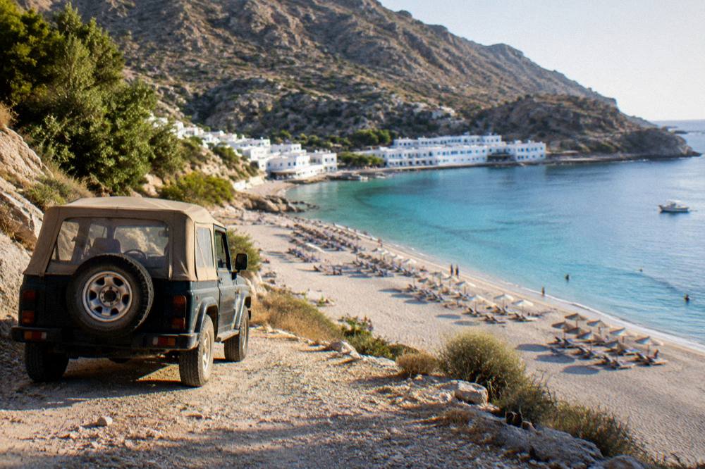 A jeep parked on a rough track above a wide sandy beach with sunloungers laid out