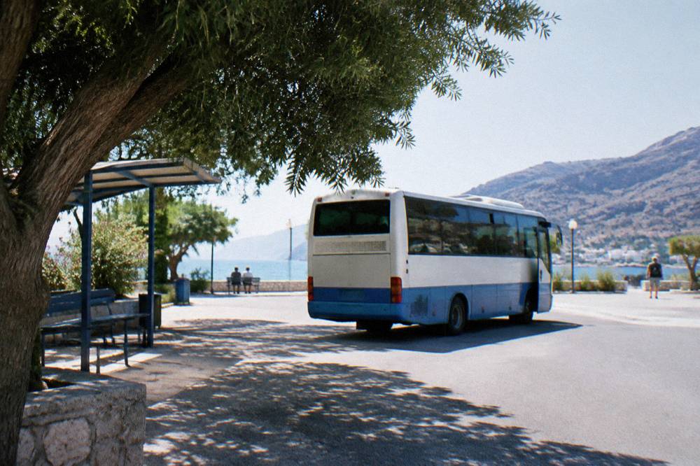 A regional bus parked at a small Greek bus station on a sunny morning