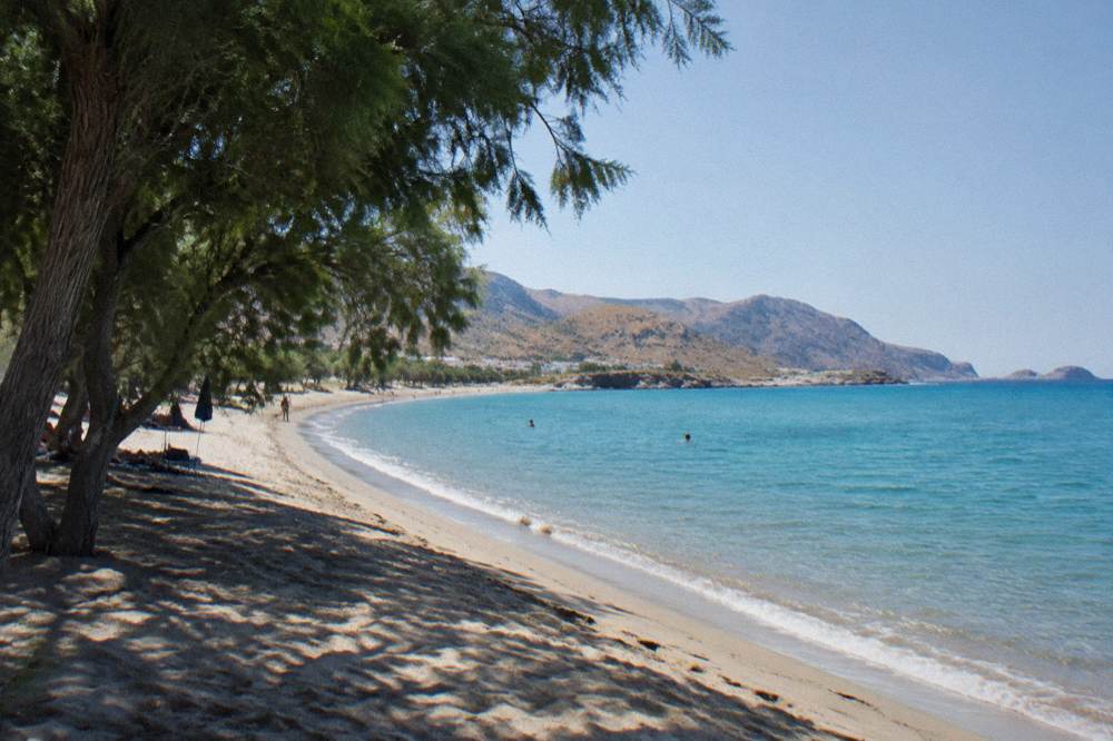 A wide sandy beach on a Greek island curving along turquoise water under a clear sky