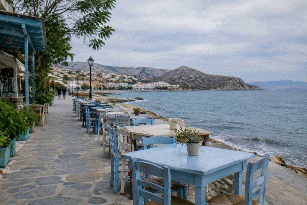 Tables and chairs set out along a seaside promenade in a small Greek coastal town