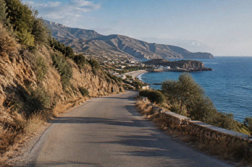 A coastal road winding through dry hills toward the sea in western Crete
